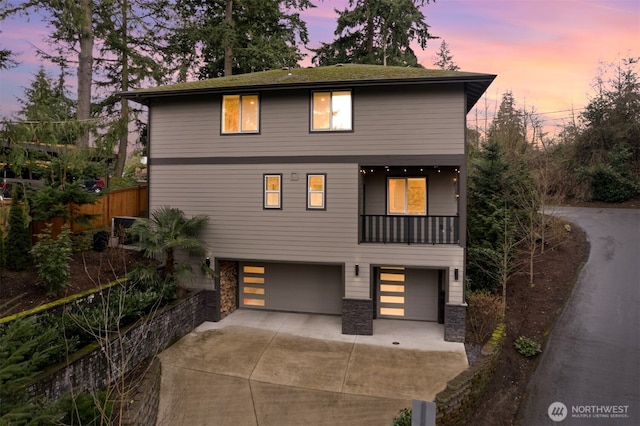 view of front of property featuring stone siding, an attached garage, concrete driveway, and fence