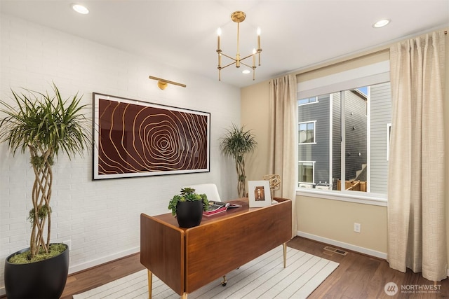 office space with an inviting chandelier, brick wall, visible vents, and wood finished floors