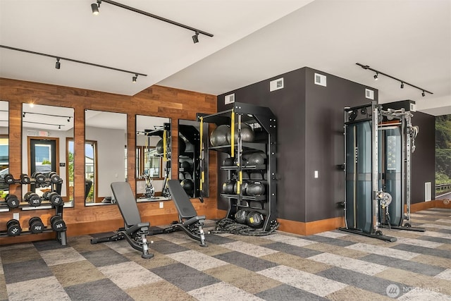 exercise room with rail lighting, visible vents, and wood walls