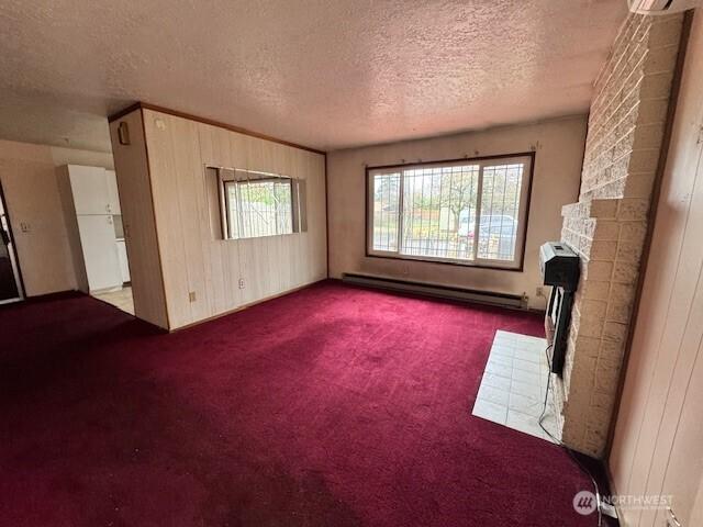 unfurnished living room featuring a baseboard heating unit, carpet, a brick fireplace, and a textured ceiling