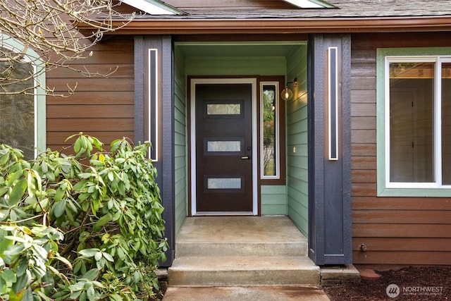 view of exterior entry with roof with shingles