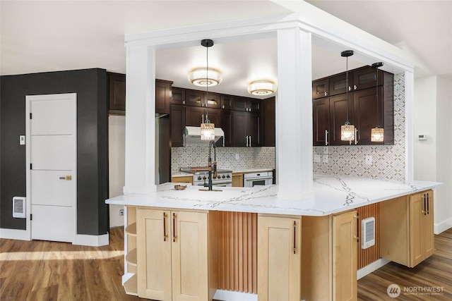 kitchen with tasteful backsplash, wood finished floors, light stone counters, a peninsula, and exhaust hood