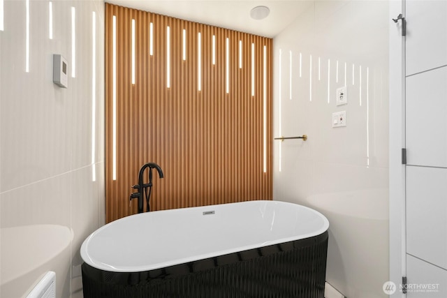 bathroom featuring a soaking tub, toilet, and tile walls