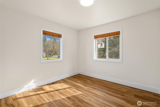 unfurnished room featuring a wealth of natural light, visible vents, baseboards, and wood finished floors