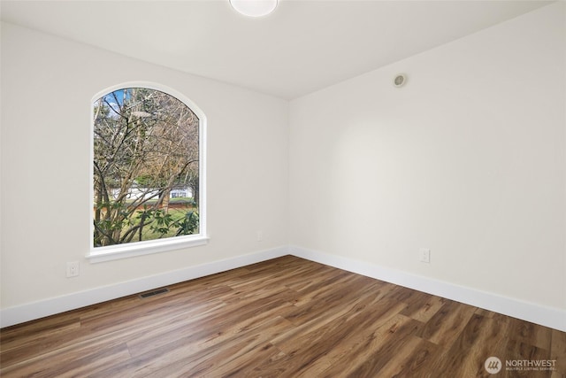 spare room with a wealth of natural light, visible vents, baseboards, and wood finished floors