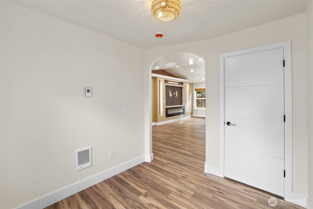 empty room featuring visible vents, baseboards, lofted ceiling, light wood-style floors, and arched walkways