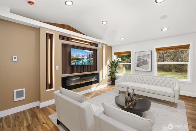 living area with visible vents, wood finished floors, a glass covered fireplace, and vaulted ceiling