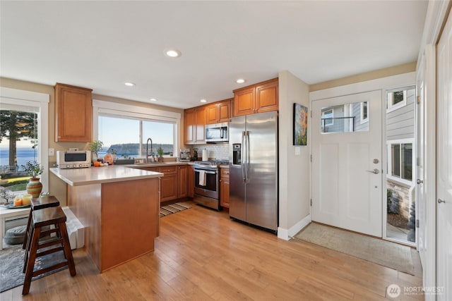 kitchen with brown cabinets, appliances with stainless steel finishes, light wood-style floors, a peninsula, and a kitchen bar