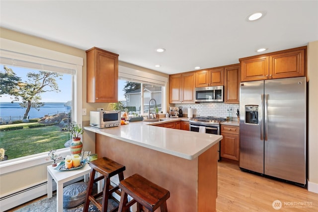 kitchen featuring a peninsula, stainless steel appliances, light countertops, a baseboard heating unit, and a sink