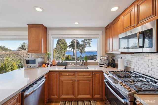 kitchen with light countertops, decorative backsplash, appliances with stainless steel finishes, brown cabinetry, and a sink