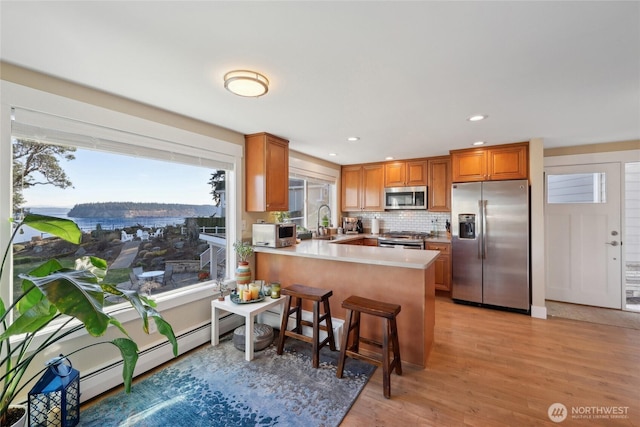 kitchen with stainless steel appliances, a peninsula, a sink, light wood-type flooring, and brown cabinetry