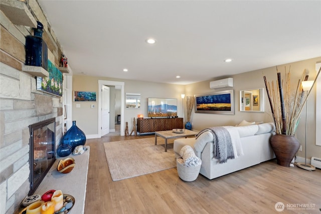 living room featuring baseboards, wood finished floors, a wall mounted air conditioner, a stone fireplace, and recessed lighting