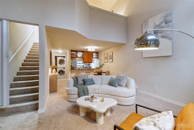 carpeted living room featuring stacked washer / dryer, stairway, baseboards, and a towering ceiling