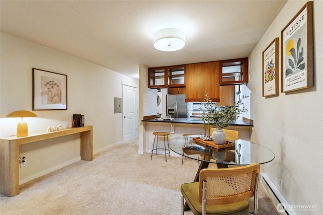 kitchen with stainless steel refrigerator with ice dispenser, a baseboard heating unit, dark countertops, brown cabinetry, and light colored carpet