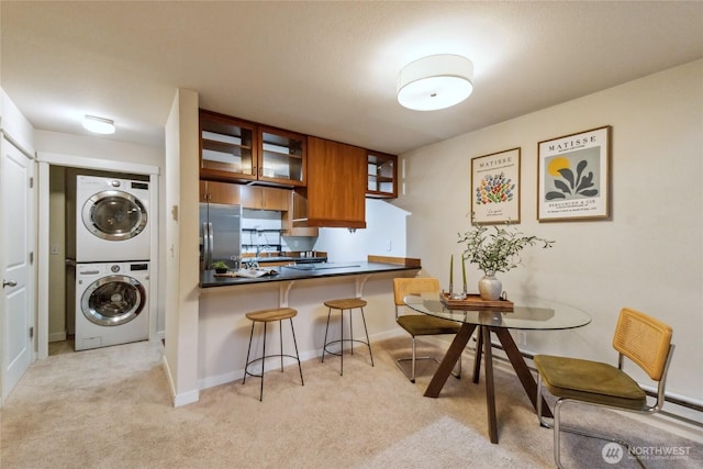 kitchen with brown cabinetry, stainless steel fridge, light colored carpet, and stacked washer / drying machine