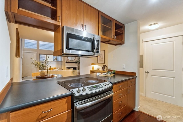 kitchen featuring glass insert cabinets, dark countertops, brown cabinetry, and stainless steel appliances