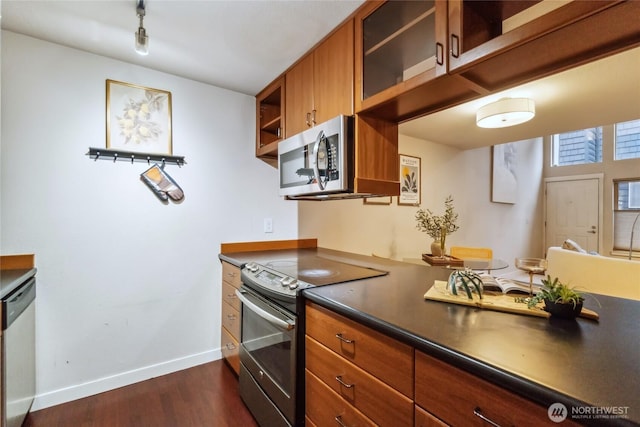 kitchen featuring dark wood-type flooring, glass insert cabinets, appliances with stainless steel finishes, dark countertops, and brown cabinets