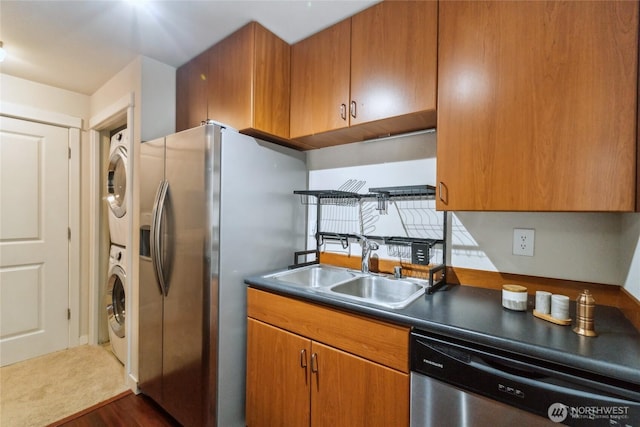 kitchen featuring brown cabinetry, stainless steel appliances, stacked washing maching and dryer, and a sink