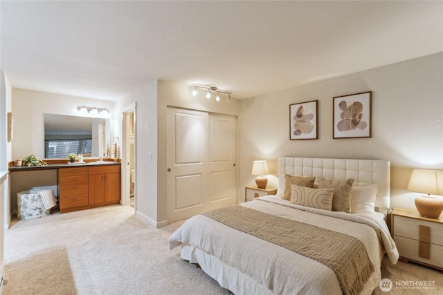 bedroom with a closet, light carpet, baseboards, and ensuite bath