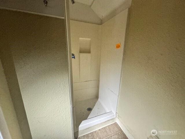 bathroom with a textured wall, a shower stall, and tile patterned floors