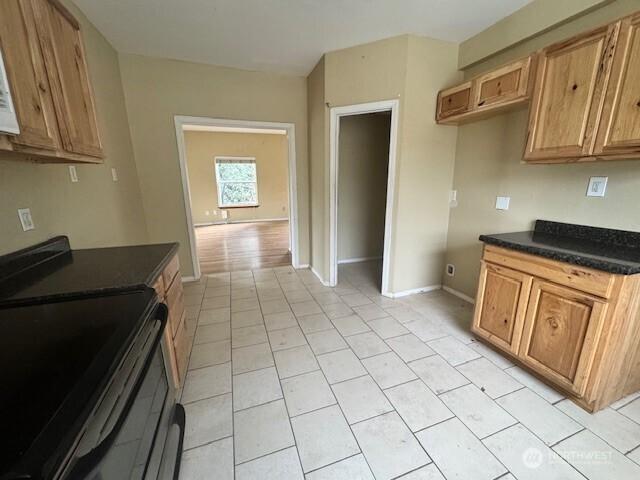 kitchen with baseboards, dark countertops, brown cabinets, black electric range oven, and light tile patterned flooring