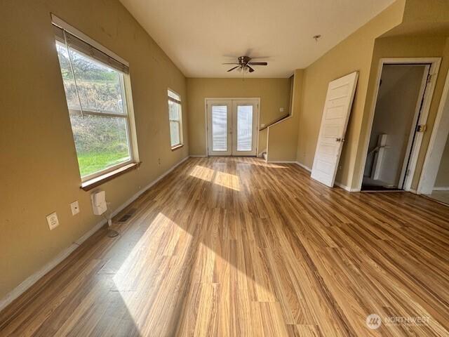 unfurnished living room featuring french doors, light wood-type flooring, and baseboards