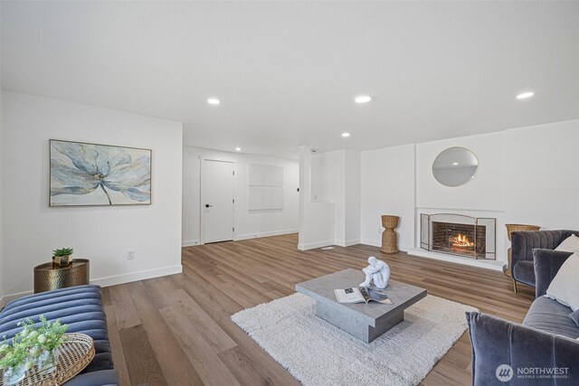 living room with recessed lighting, a lit fireplace, baseboards, and wood finished floors