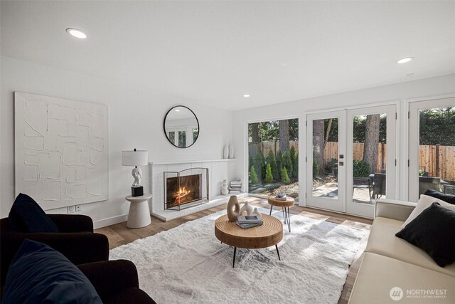 living area featuring baseboards, wood finished floors, french doors, a brick fireplace, and recessed lighting