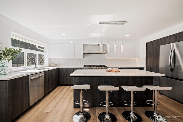 kitchen featuring a breakfast bar area, light countertops, appliances with stainless steel finishes, wall chimney range hood, and modern cabinets