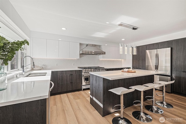 kitchen with wall chimney range hood, modern cabinets, appliances with stainless steel finishes, and a sink