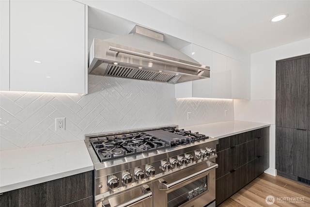 kitchen featuring white cabinets, light countertops, wall chimney range hood, double oven range, and modern cabinets