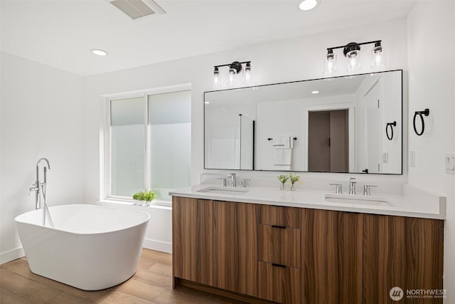 bathroom with a freestanding bath, wood finished floors, a sink, and visible vents