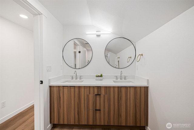 full bath featuring double vanity, wood finished floors, a sink, and baseboards