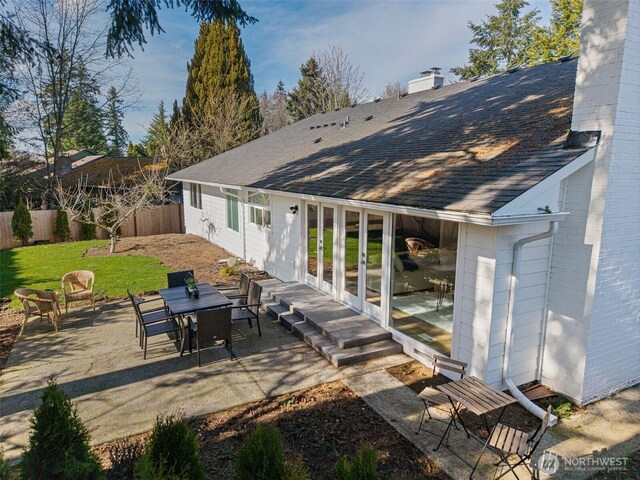 rear view of house featuring brick siding, roof with shingles, a chimney, a patio area, and fence