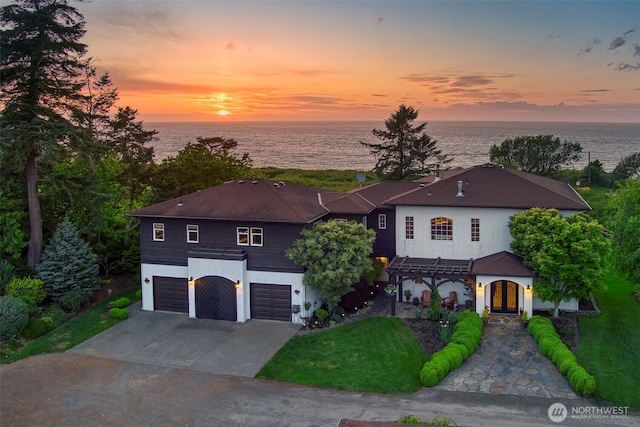 view of front of home with a water view, concrete driveway, stucco siding, an attached garage, and a pergola