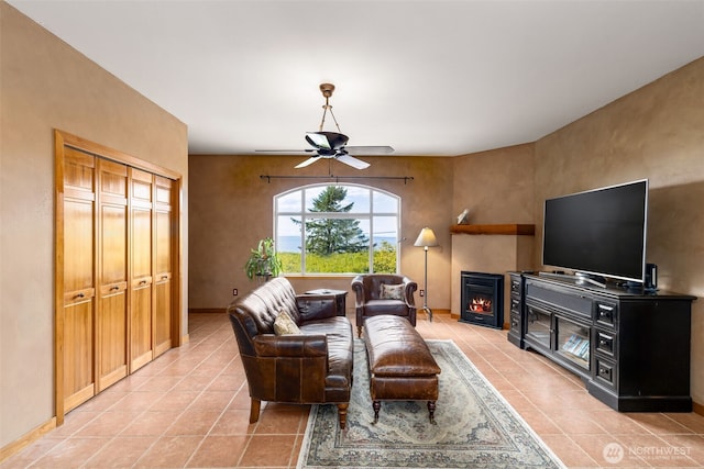 1939 49th St, Port Townsend, WA 98368 - living room featuring light tile patterned floors, a ceiling fan, a warm lit fireplace, and baseboards