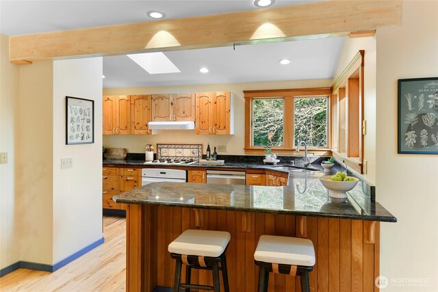 kitchen with a skylight, white oven, a sink, light wood-type flooring, and under cabinet range hood