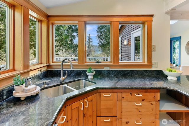 kitchen with lofted ceiling, dark stone counters, a sink, and a wealth of natural light