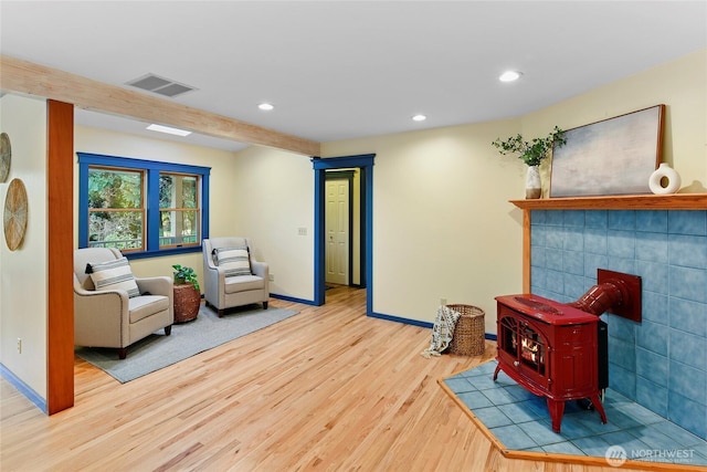 living area featuring recessed lighting, wood finished floors, visible vents, baseboards, and a wood stove