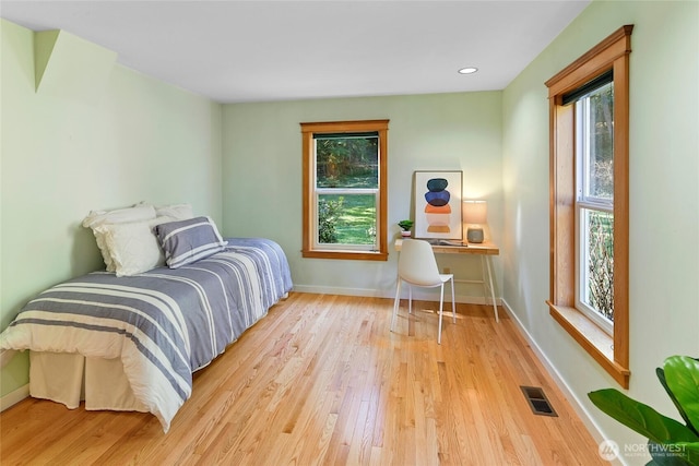 bedroom with multiple windows, wood finished floors, visible vents, and baseboards