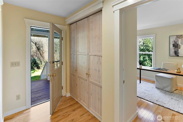 doorway with light wood-style floors, baseboards, and a wealth of natural light