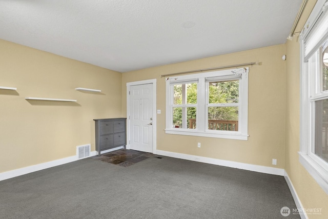 interior space with dark colored carpet, visible vents, baseboards, and a textured ceiling