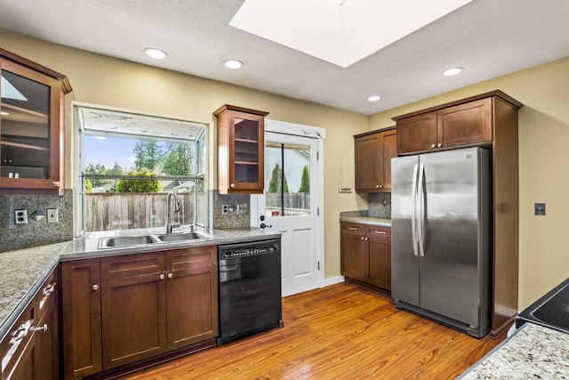 kitchen with a skylight, freestanding refrigerator, a sink, dishwasher, and light wood-type flooring