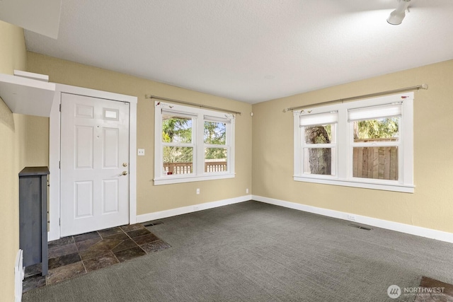 foyer entrance featuring dark colored carpet, visible vents, and baseboards