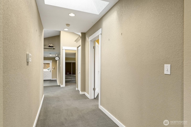 corridor featuring a skylight, a textured wall, baseboards, and carpet floors