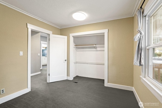 unfurnished bedroom with ornamental molding, a textured ceiling, a closet, dark colored carpet, and baseboards