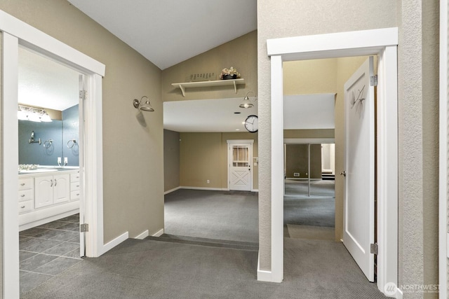 hallway with vaulted ceiling, carpet flooring, baseboards, and a sink