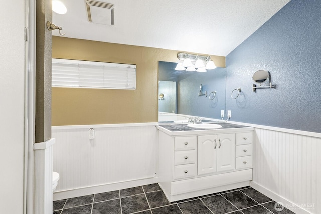 bathroom with visible vents, a wainscoted wall, toilet, a textured wall, and vanity