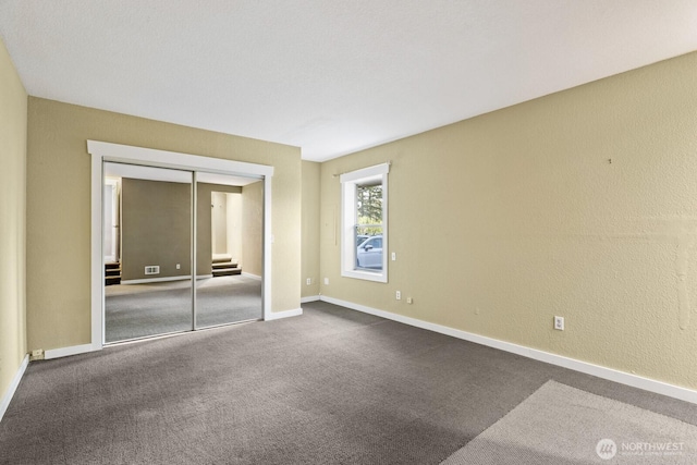 unfurnished bedroom with dark colored carpet, a closet, baseboards, and a textured wall