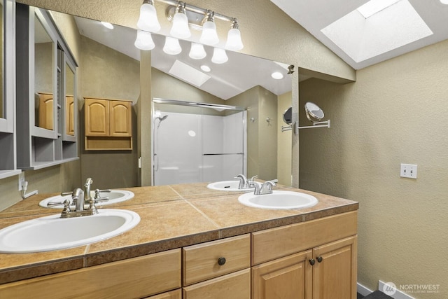 bathroom with double vanity, vaulted ceiling with skylight, a stall shower, a textured wall, and a sink